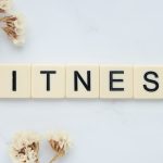 Close-up of scrabble tiles spelling 'FITNESS' on a marble surface with white flowers.